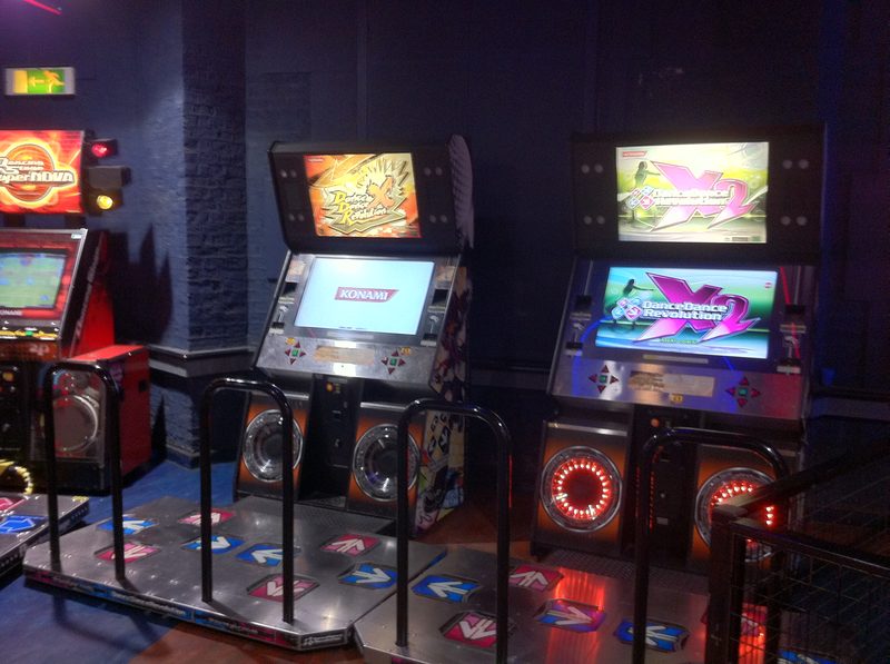 Two North American Dance Dance Revolution X series arcade cabinets with dance stages in an arcade