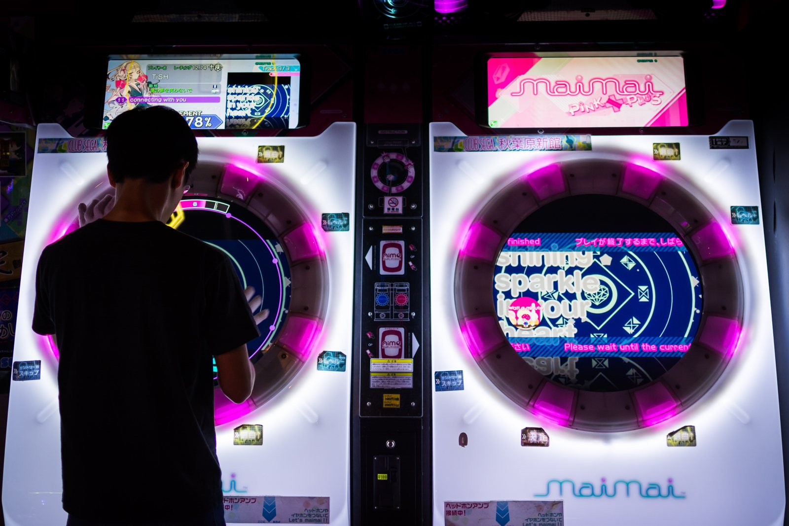 A player playing a maimai PiNK PLUS arcade cabinet in Japan