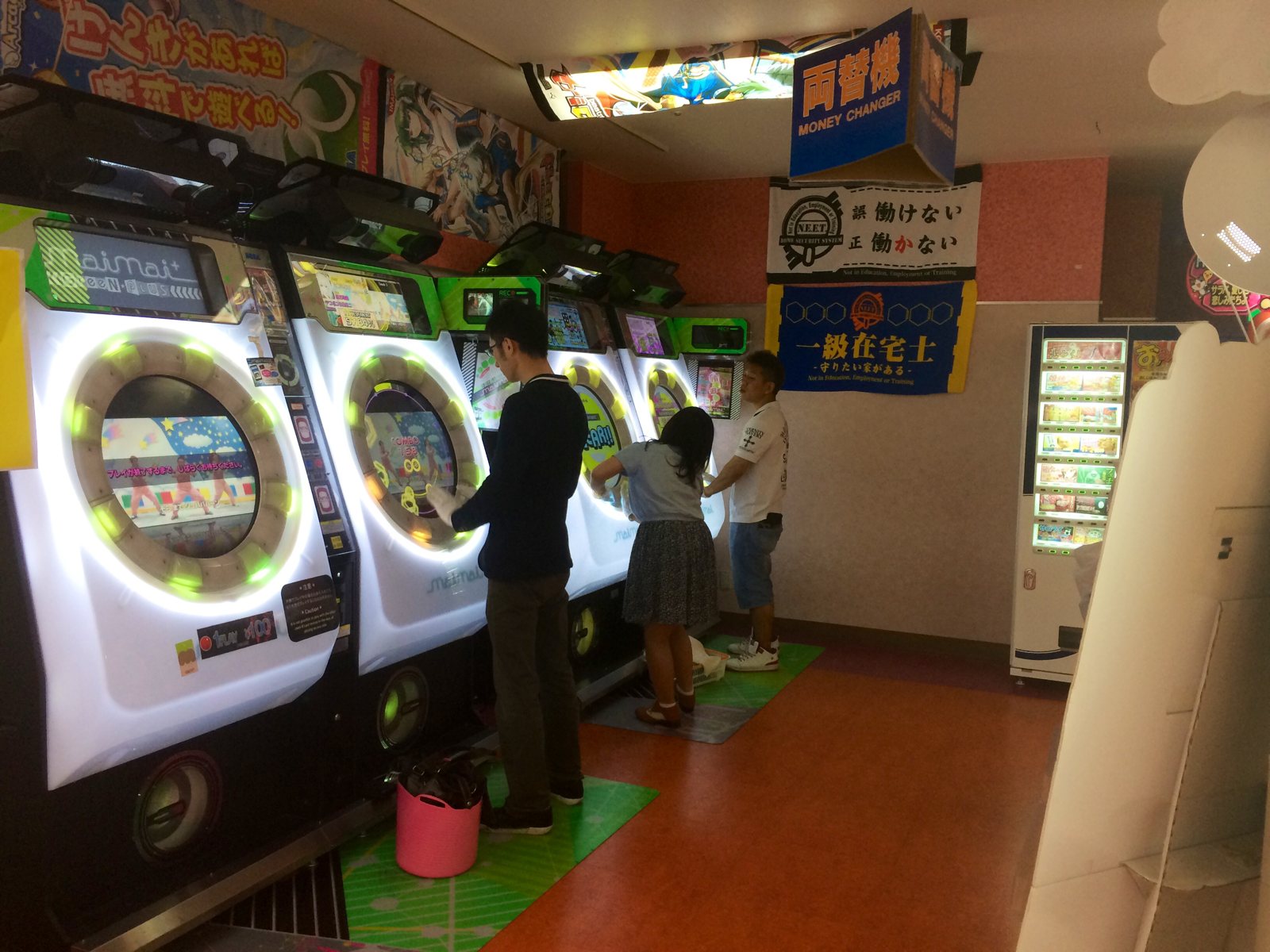 Three players playing maimai GreeN PLUS arcade cabinets in Japan